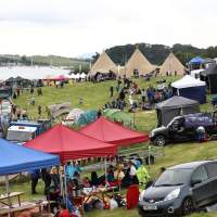 Gazebos, cars and visitors are in the foreground with a three Tipi set up in the distance