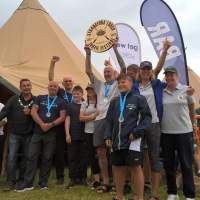 Rowers cheer and pose for a photo, holding up a circular award, Two tipis are behind them