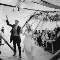 Bride and groom cheer as the walk through seated guests inside their wedding Tipi