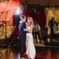 The bride and groom have their first dance inside their wedding Tipi, fairylit panels and a band are behind them