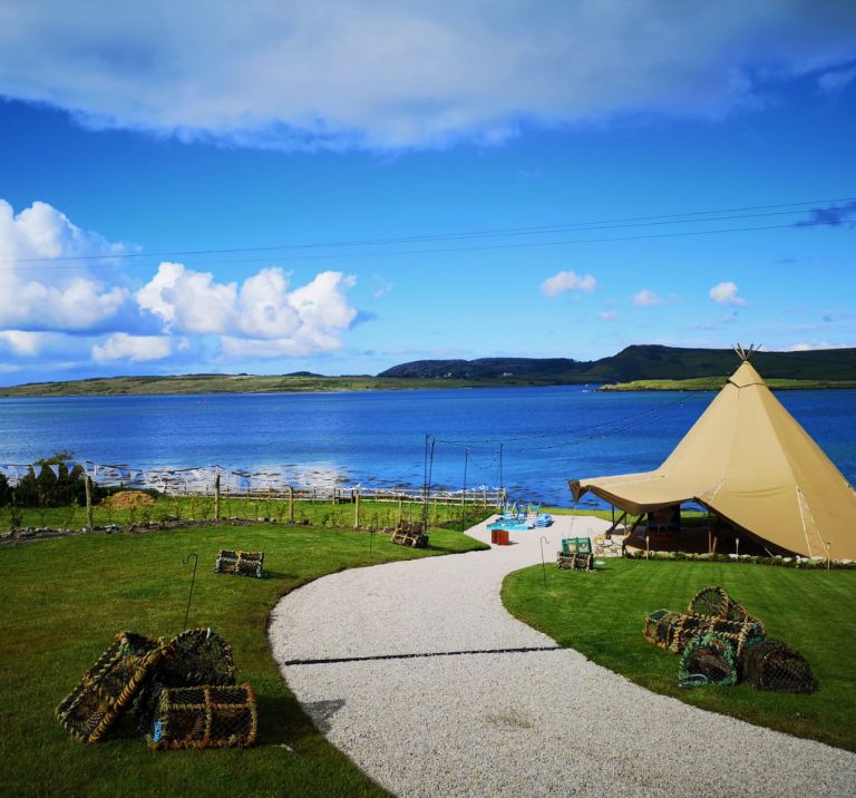 A ceremony tipi is set up on the coast of Donegal, Ireland, with gorgeous blue waters and sky in the background.