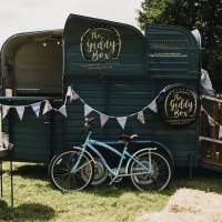 A horsebox champagne bar is decorated with bunting, a blue vintage bike sits in front and a drinks tray holding glasses