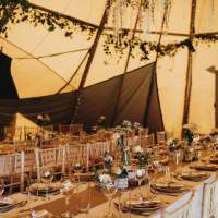 Tables and chairs sit in rows, with rustic decorations and natural foliage inside the Tipi