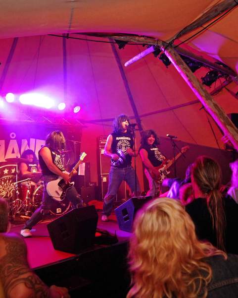 A rock band plays inside a festival tipi, crowds gather round the stage and it is lit up with purple lights