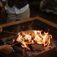 Wedding guests toast marshmallow over the top of magnakata's open firepits