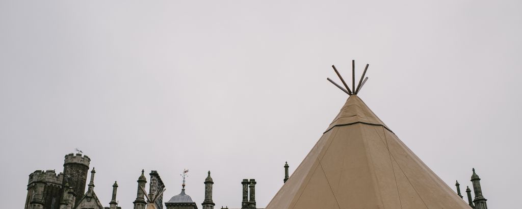 Two tipi tops are highlighted against a grey sky, the top of Narrow Water Castle stands behind them