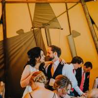 The bride and groom stand together with their arms around each other inside their tipi wedding reception
