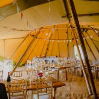 Simple decorations inside three tipis, colourful bunting lines the roof with long wooden tables and chivari chairs