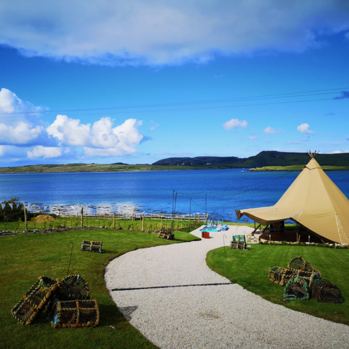 A ceremony tipi is set up on the coast of Donegal, Ireland, with gorgeous blue waters and sky in the background.