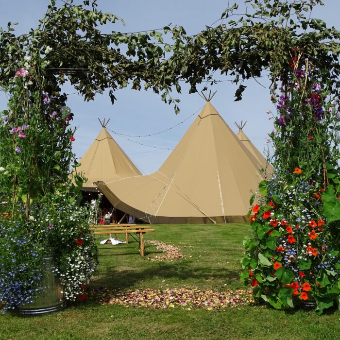 Three tipi wedding setup in an open field with a beautiful DIY floral square arch