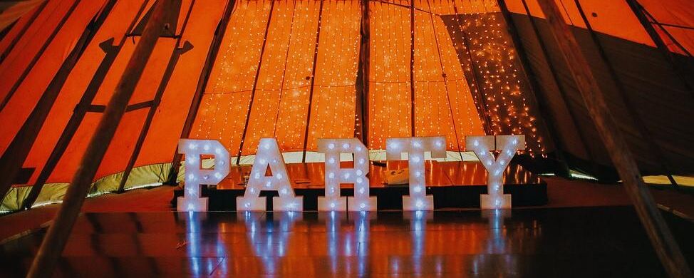 Large Lettered Lights spelling out Party stand in front of staging inside a tipi
