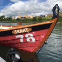 A red Skiff sits on the water on Strangford Lough, Tipis and Delamont Country Park are in the background
