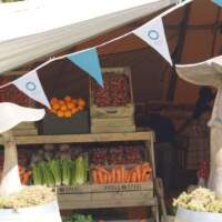 Two wooden mushrooms sit ontop of old whiskey barrels in front of a tipi displaying fruit and vegetables