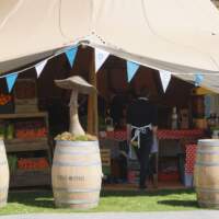 Decorative Wooden mushrooms sit ontop of old whiskey barrels in front of the six Tipi Festival set up at Odaios Food Fair
