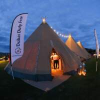 Three Tipis are joined in a row with festoon lighting at their tops, Dubai Duty Free flags stand either side of the entrance
