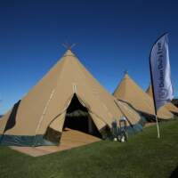 Three Tipis are joined in a row on green grass, Dubai Duty Free flags stand either side of the entrance