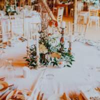 A round table is decorated with rustic foliage and four candle silver candlesticks