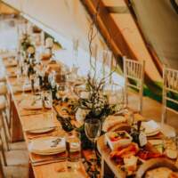 Long wooden tables are decorated with flowers and candles in a rustic manner, chairs sit either side
