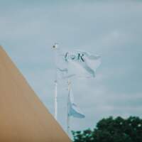 Two baby blue flags with L & R on them flap against the wind beside a tipi