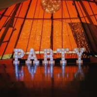 Large Lettered Lights spelling out Party stand in front of staging inside a tipi