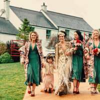 The bride, bridesmaids and flower girl hold hands while they walk down to the tipi wedding reception tent