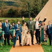 The wedding party pose for a fun photograph in front of a wedding tipi