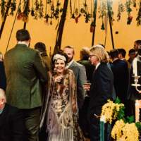 The guests stand facing away towards the bar, the bride holds a drink and smiles facing the camera