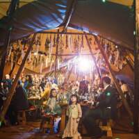 A little girl looks up at dried flowers hanging from the crossbeams of the tipi, guests sit and laugh in the background