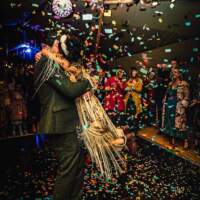 The groom swings the bride around on the dancefloor, coloured confetti falls around them