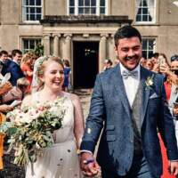 The bride and groom hold hands and walk through their wedding guests in front of their family estate in Portstewart