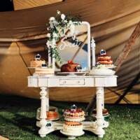 A vintage cream dresser holds multiple cakes inside a tipi wedding