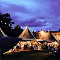Three tipi set up at night with festoon lighting, open sides show wedding guests in Portstewart Northern Ireland