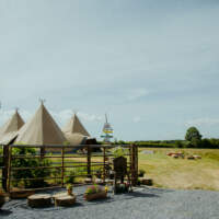 Three tipi wedding in a field, with a handmade wooden signpost and metal fencing in front