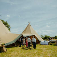 Guest arrive at a three tipi wedding set up, tables and bbq's stand outside beside the tipi entrance