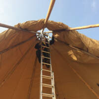 A Magnakata crew member is on a ladder fixing the Tipi canvas in place at the central poles