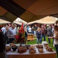Corporate guests surround a buffet table in a ring of six open sided Tipis, a firepit sits in the middle