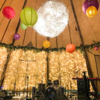 A Tipi is dressed for a birthdy party with fairlight panels, foliage and colourful paper lanterns hanging from the roof