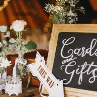 A framed blackboard saying cards & gifts stands with flowers sitting in jamjars decorated with lace
