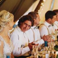 The wedding party sit at a table, clap and smile
