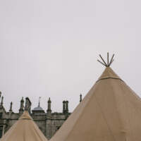 Two tipi tops are highlighted against a grey sky, the top of Narrow Water Castle stands behind them