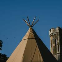 A top of a Tipi stands in front of Narrow Water Castle with a bright blue sky in the background