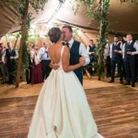 Bride and Groom dance and kiss on a wooden dancefloor with guests surrounding them inside their Tipi Wedding