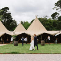 Bride & groom walk together in front of four linked tipis set up on the grounds of Mount Stewart