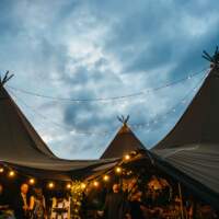 Three tipis are joined their central poles highlighted by the sky, festoon lighting hangs creating a cosy atmosphere