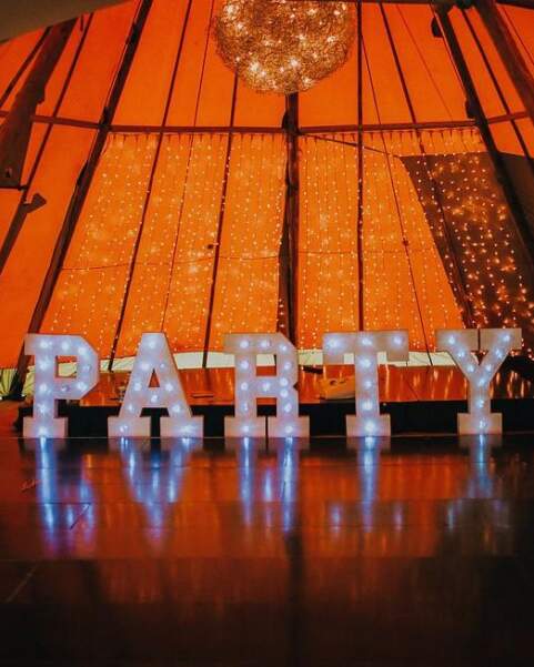 Large Lettered Lights spelling out Party stand in front of staging inside a tipi
