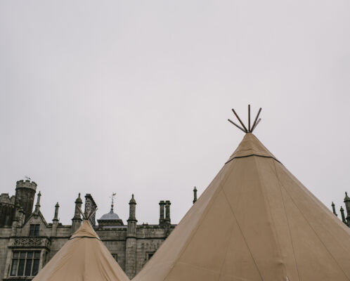 Two tipi tops are highlighted against a grey sky, the top of Narrow Water Castle stands behind them