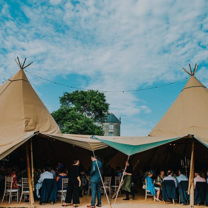 Open sided entrance to a five tipi wedding reception, inside is crowded with guests sitting at tables