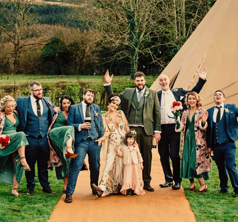 The wedding party pose for a fun photograph in front of a wedding tipi