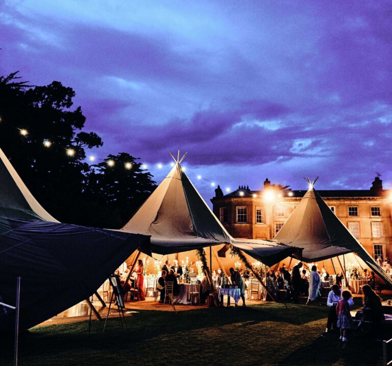 Three tipi set up at night with festoon lighting, open sides show wedding guests in Portstewart Northern Ireland
