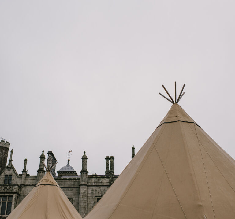 Two tipi tops are highlighted against a grey sky, the top of Narrow Water Castle stands behind them